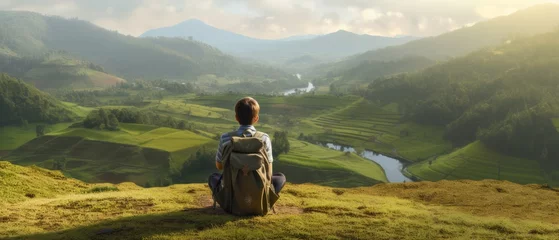 Tuinposter Tourist with backpack sitting on top of hill in grass field and enjoying beautiful landscape view. Rear view of teenage boy hiker resting in nature. Active lifestyle. Concept of local travel. Banner © Natalja