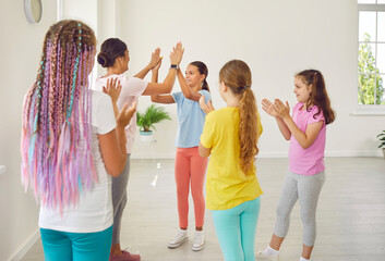 Female friendly choreographer or sports trainer giving high five to happy smiling kids students girls in choreography studio after doing dance workout. Children sport and active lifestyle concept.