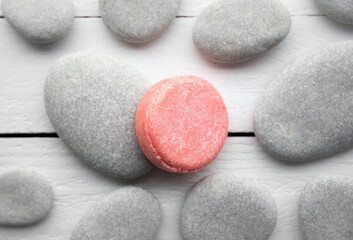 Flat lay view of pink color solid shampoo bar, conditioner bar on flat sea stones. Minimalist beauty set indoors. Shallow depth of field.
