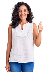 Middle age beautiful woman wearing casual sleeveless t shirt smiling happy and positive, thumb up...