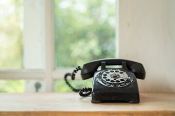 A vintage dial rotary nostalgia telephone which is placed on wooden table and window background....