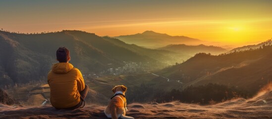 Man with beard and his small yellow dog enjoying mountain sunset and looking at the distance. - obrazy, fototapety, plakaty