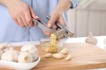 Woman squeezing garlic with press at wooden table indoors, closeup - obrazy, fototapety, plakaty