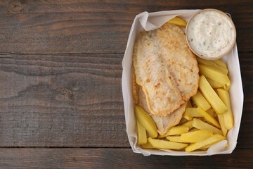 Delicious fish and chips with tasty sauce in paper box on wooden table, top view. Space for text