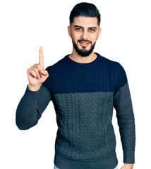 Young arab man with beard wearing casual sweater smiling with an idea or question pointing finger up with happy face, number one