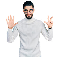 Naklejka premium Young arab man with beard wearing elegant turtleneck sweater and glasses showing and pointing up with fingers number eight while smiling confident and happy.
