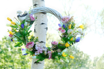 beautiful decorative Spring wreath hanging in garden, natural background. symbol of Beltane holiday. festive decor for spring - obrazy, fototapety, plakaty