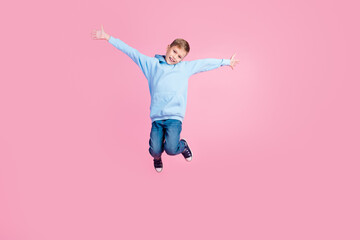 Full length portrait of overjoyed cheerful schoolkid jump raise hands empty space isolated on pink...