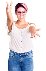 Young beautiful woman with pink hair wearing casual clothes and glasses looking at the camera smiling with open arms for hug. cheerful expression embracing happiness.