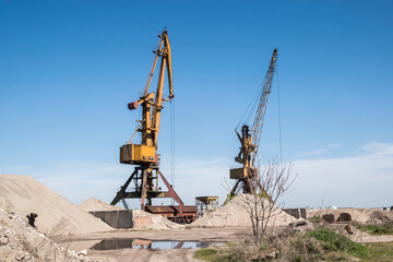 Fototapeta na wymiar Port industrial cranes at river sand unloading depot on clear sunny day