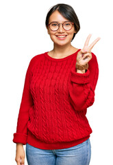 Young beautiful hispanic woman with short hair wearing casual sweater and glasses showing and pointing up with fingers number two while smiling confident and happy.