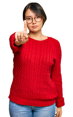 Young beautiful hispanic woman with short hair wearing casual sweater and glasses pointing with finger up and angry expression, showing no gesture