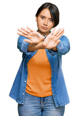 Young beautiful hispanic woman with short hair wearing casual denim jacket rejection expression crossing arms and palms doing negative sign, angry face