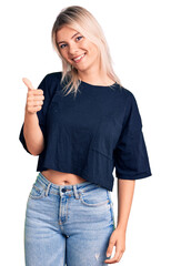 Young beautiful blonde woman wearing casual t-shirt doing happy thumbs up gesture with hand. approving expression looking at the camera showing success.