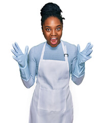 Young african american woman wearing apron celebrating victory with happy smile and winner expression with raised hands