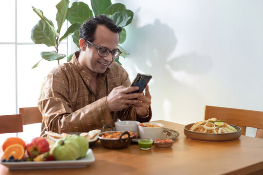 Indian man wearing traditional cloth uses smartphone while waiting for food, Indian food