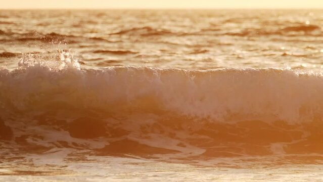 Breaking ocean wave on sunset backlit with sun. Fonte da Telha, Costa da Caparica, Portugal. Slow motion