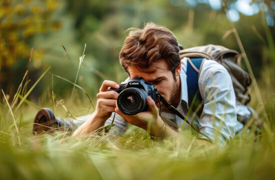 A handsome photographer is lying on the ground, holding his camera and taking photos of wildlife in nature.
