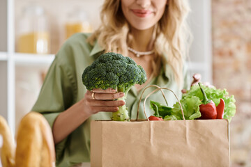 A woman holding a paper bag filled with various fresh vegetables in a kitchen.