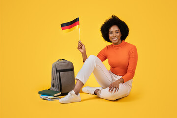 Happy young woman with afro hair proudly holding the German flag, sitting cross-legged beside