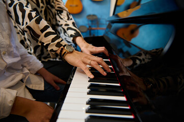 Close-up woman teacher hands touching piano keys while playing grand piano with her student boy in...