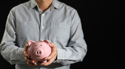 Business man hand hold piggy bank on black background with copy space, business investment and money saving concept