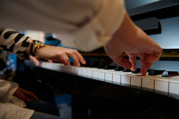 Musician boy playing grand piano during music lesson, performing classical melody, creating and feeling the rhythm of sounds while putting fingers on white and black piano keys. Close-up bottom view.