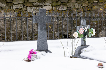 A serene winter scene unfolds in the small cemetery, where snow blankets the ground and clings to the gravestones. 