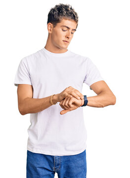 Young handsome man wearing casual white tshirt checking the time on wrist watch, relaxed and confident
