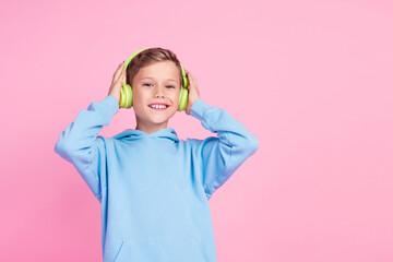 Portrait of sweet small boy toothy smile hands touch headphones empty space isolated on pink color...