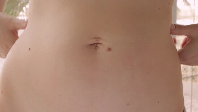 close-up of a woman examining  skin on her abdomen. She is focusing on  problem of sagging skin and cellulite