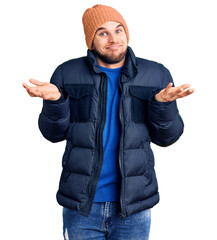 Young handsome man wearing winter clothes clueless and confused expression with arms and hands...