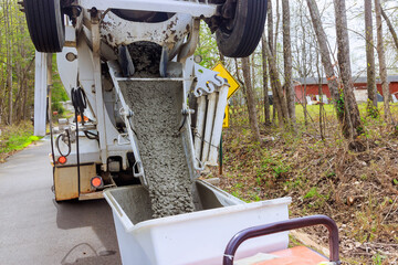 Wet cement coming down cement truck chute into a wheelbarrow track concrete buggy at construction...
