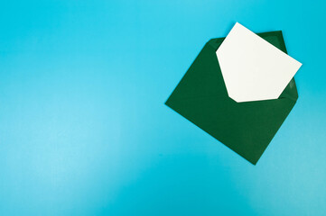 Top view of dark green envelope, white card on blue background. Post flat lay. Copy space.