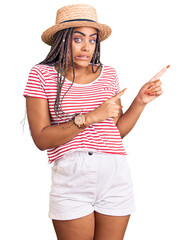 Young african american woman with braids wearing summer hat pointing aside worried and nervous with...