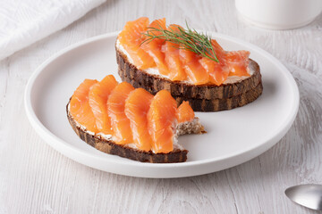 Rye sandwich with salmon and cream cheese on white wooden table