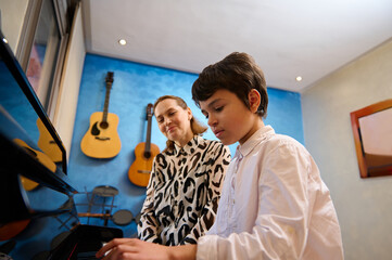 Talented teenager boy musician having a piano lesson with his teacher. Female pianist explaining...