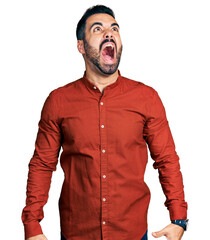 Young hispanic man with beard wearing casual shirt angry and mad screaming frustrated and furious, shouting with anger. rage and aggressive concept. - obrazy, fototapety, plakaty