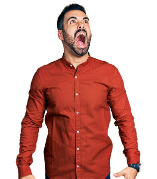 Young hispanic man with beard wearing casual shirt angry and mad screaming frustrated and furious, shouting with anger. rage and aggressive concept.