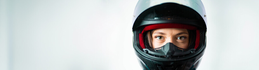 female motorcyclist in a helmet and motorcycle jacket against a white wall