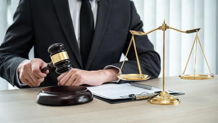 A male lawyer or notary working with contract papers, book and wooden gavel on table in courtroom,...