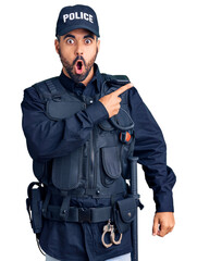 Young hispanic man wearing police uniform surprised pointing with finger to the side, open mouth amazed expression. - obrazy, fototapety, plakaty