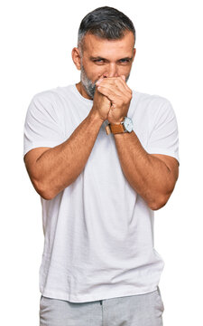 Middle age handsome man wearing casual white tshirt laughing nervous and excited with hands on chin looking to the side