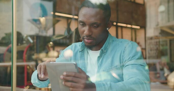 Portrait of young man working with digital computer and financial papers with stylish beard which sitting near the window of street coffee shop