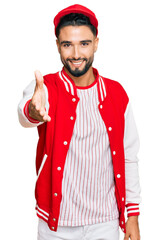 Young man with beard wearing baseball uniform smiling friendly offering handshake as greeting and welcoming. successful business.