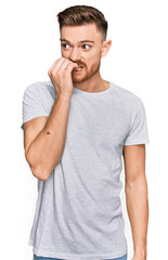 Young redhead man wearing casual grey t shirt looking stressed and nervous with hands on mouth biting nails. anxiety problem.