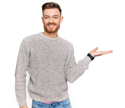 Young redhead man wearing casual winter sweater smiling cheerful presenting and pointing with palm of hand looking at the camera.