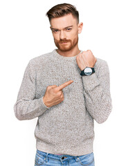 Young redhead man wearing casual winter sweater in hurry pointing to watch time, impatience, looking at the camera with relaxed expression