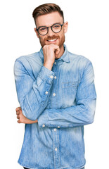 Young redhead man wearing casual denim shirt looking confident at the camera with smile with crossed arms and hand raised on chin. thinking positive.