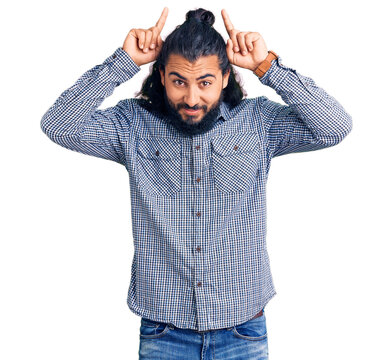 Young arab man wearing casual clothes doing funny gesture with finger over head as bull horns